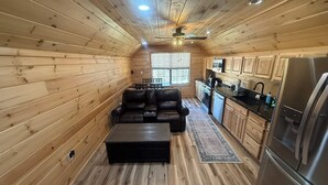 Un intérieur de chalet en bois compact, comprenant un canapé, une table basse, un coin cuisine et un réfrigérateur.