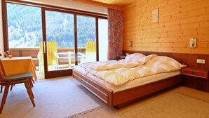 Ein Schlafzimmer mit Holzvertäfelung, einem großen Bett, einem Sessel, einem Tisch und Blick auf eine verschneite Landschaft durch eine Schiebetür.