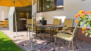 Eine Terrasse im Freien mit einem Steintisch, Stühlen und einem großen Sonnenschirm.