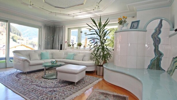Ein geräumiges Wohnzimmer mit einem weißen Sofa, einem Glastisch und einer großen Pflanze.