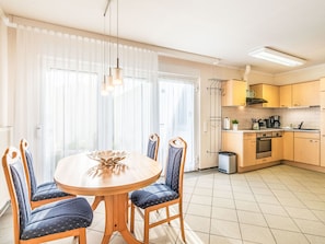 A dining area with a round table and chairs, a kitchen with wooden cabinets, and a radiator. - Apartment 3 by Interhome (Bansin)