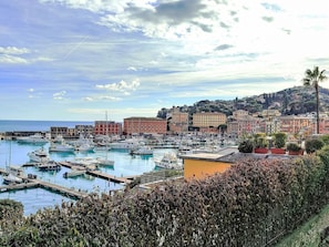 Una marina amb vaixells amarrats, un passeig marítim i edificis colorits al fons.