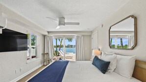 Una camera d'albergo con un letto, una ventola a soffitto, una televisione, una finestra con tende e vista sull'oceano.
