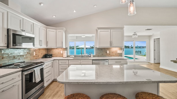 A modern kitchen with a large island, stainless steel appliances, and a view of the ocean. - Waterfront 4 BR Home, Pool, Private Dock, Kayaks, Putting Green, Walk to Beach (Indian Rocks Beach)