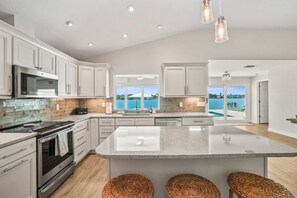 A modern kitchen with a large island, stainless steel appliances, and a view of the ocean. - Waterfront 4 BR Home, Pool, Private Dock, Kayaks, Putting Green, Walk to Beach (Indian Rocks Beach)