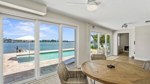 A room with a wooden table, wicker chairs, and large sliding glass doors leading to a pool area with a view of the water. - Waterfront 4 BR Home, Pool, Private Dock, Kayaks, Putting Green, Walk to Beach (Indian Rocks Beach)