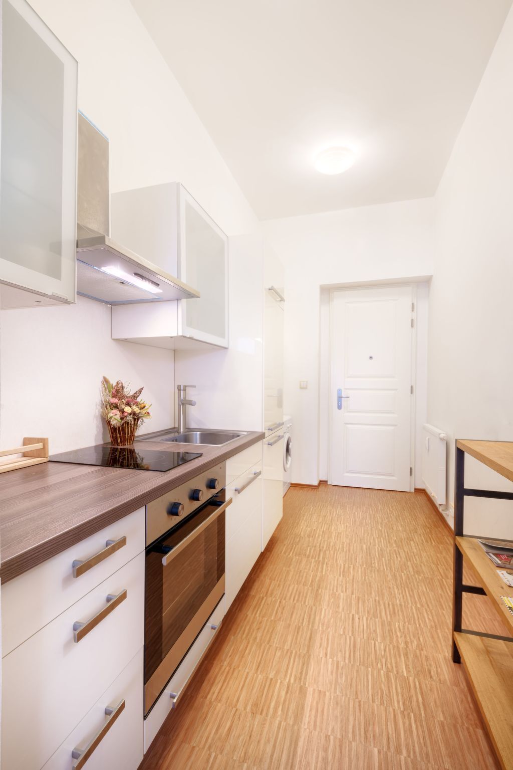 Une cuisine de taille réduite avec des meubles blancs, un plan de travail en bois, des appareils en acier inoxydable et un plancher en bois.