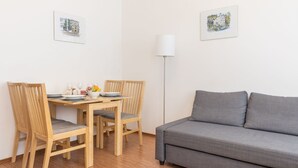 Un coin repas avec une table en bois, quatre chaises et un canapé gris. Deux tableaux encadrés ornent le mur.