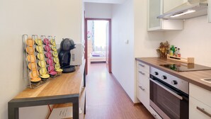 Un couloir étroit mène à une chambre qui contient un lit et une fenêtre. On aperçoit, sur la droite, un coin cuisine avec une cuisinière, un évier et un plan de travail.