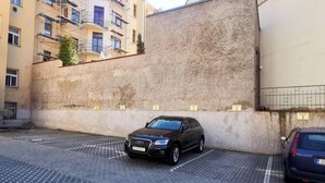 Une voiture noire est garée sur un parking dont le mur est texturé et les places de stationnement sont numérotées.