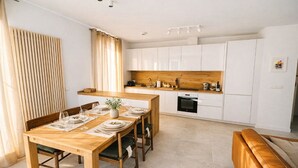 Cozinha moderna com armários brancos, bancada de madeira e área de refeições com mesa e cadeiras de madeira.
