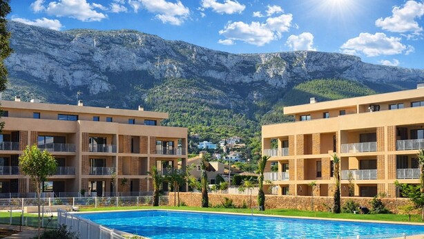 Um hotel com piscina, várias varandas e montanhas ao fundo.
