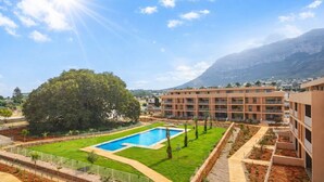Um edifício moderno com piscina, rodeado por vegetação e montanhas ao fundo.