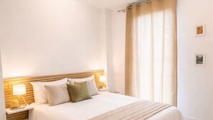 Quarto com uma cama grande, mesa de cabeceira com abajur, ventilador de teto e janela com cortinas.