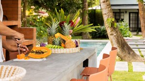A bar area with a concrete countertop, a variety of tropical fruits, and a pool in the background. - Altavida Lodge · New Studio with Pool in El Valle · N5 (Valle de Anton)
