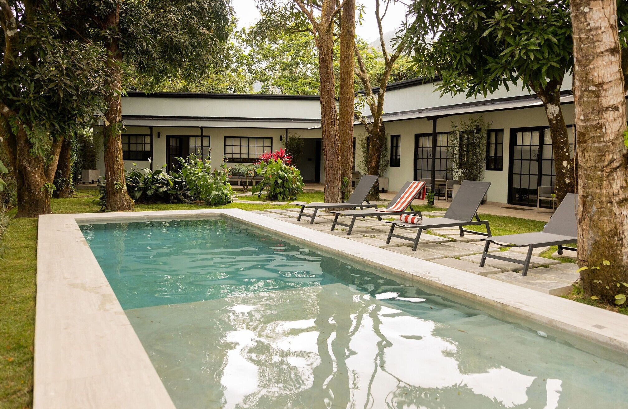 Una piscina rectangular con sillones de descanso y un edificio al fondo.