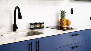 A modern kitchen with a stainless steel sink, blue cabinets, and a black faucet. There are two pineapples and a coconut on the counter. - Altavida Lodge · New Studio with Pool in El Valle · N5 (Valle de Anton)
