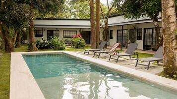 A rectangular swimming pool with lounge chairs and a building in the background.