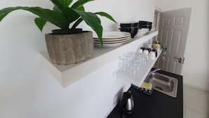 Eine Küche mit weißen Regalen, auf denen Teller, Schüsseln und Gläser stehen, eine Topfpflanze und ein Wasserkocher.