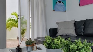 Ein modernes Wohnzimmer mit einem weißen Sofa, zwei Blumentöpfen auf einem weißen Couchtisch und Kunstwerken an den Wänden.
