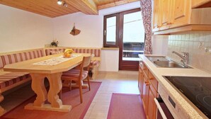 A cozy kitchen with wooden cabinets, a dining table with benches, a large window, and a built-in stove. - Apartment Heaven by Interhome (Gaschurn)