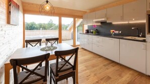 A modern kitchen with wooden cabinets, a dining table with chairs, and a hanging light fixture. - Ruhig mit einem herrlichen Blick auf die Berge. by Interhome (Schwarzenberg)