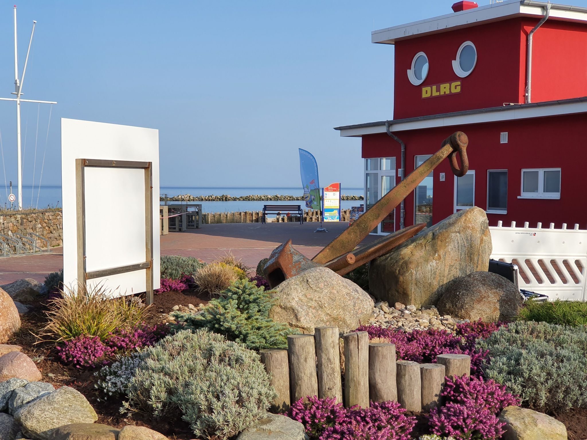 Een rood gebouw met het bord 'DLRG' en een groot, roestig anker op de voorgrond.