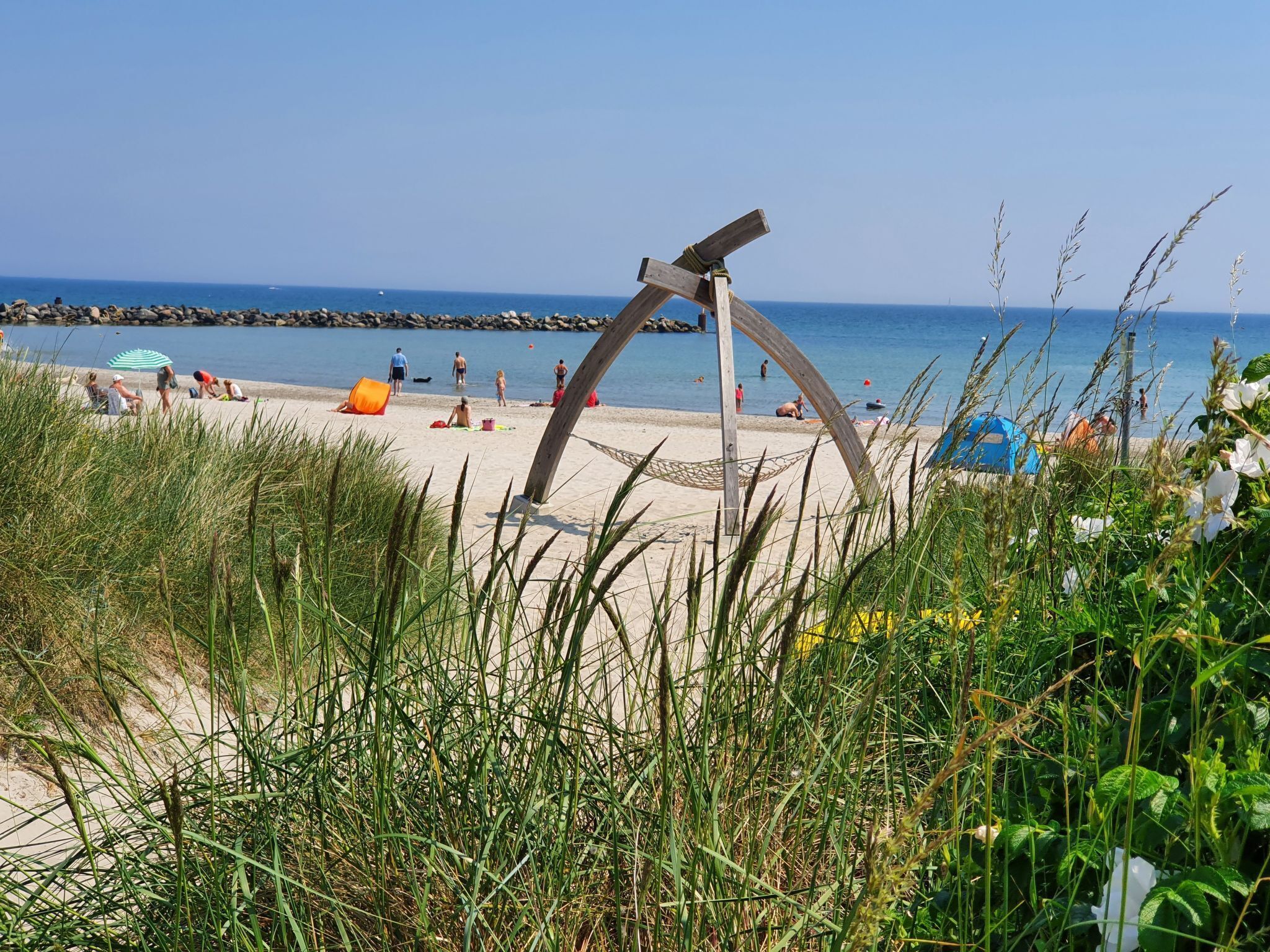 A beach with a wooden sculpture, tents, and people.