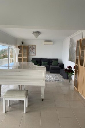 Ein geräumiges Wohnzimmer mit Klavier, einer Sofagarnitur und einem Essbereich mit Tisch und Bank.