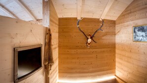 Ein Interieur einer Holzhütte mit einem aufgehängten Hirschkopf, einem Fenster und einem gerahmten Bild an der Wand.