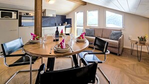 Et hyggeligt værelse med et spisebord dækket til fire personer, en sofa og et køkken i baggrunden.