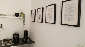 Une cuisine équipée d’une cuisinière à gaz, d’une machine à café et de documents encadrés accrochés au mur.