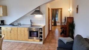 Una cucina moderna con forno a incasso, piano cottura a gas e cappa aspirante in acciaio inossidabile. C'è un'area pranzo con tavolo e sedie in legno, e un divano grigio.