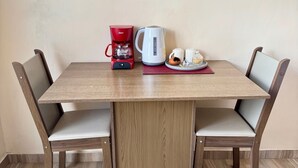 A wooden dining table with two chairs, a red coffee maker, a white electric kettle, and a small tray with a teapot and cups.