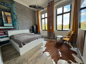 Une chambre à coucher avec un grand lit, une chaise, un radiateur et une fenêtre avec des rideaux.