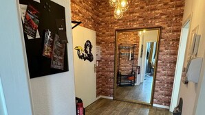A hallway with a brick wall, wooden flooring, a hanging light fixture, and a door leading to another room. - Design Apartment I by Interhome (Görlitz)