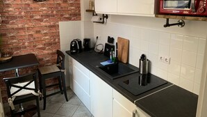A compact kitchen with a brick wall, a black clock, a red microwave, and a small dining area with a chair and table. - Design Apartment I by Interhome (Görlitz)