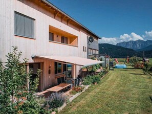 A modern two-story building with a covered patio area, a large window, and a view of mountains in the background. - Neue Ferienwohnung in Schwarzenberg mit Garten und Grill by Interhome (Schwarzenberg)