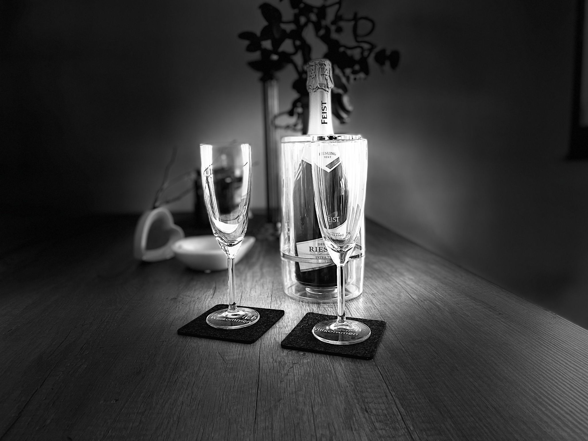Une bouteille de champagne et deux verres sur une table en bois, accompagnés de sous-verres, le tout sur un fond sombre.