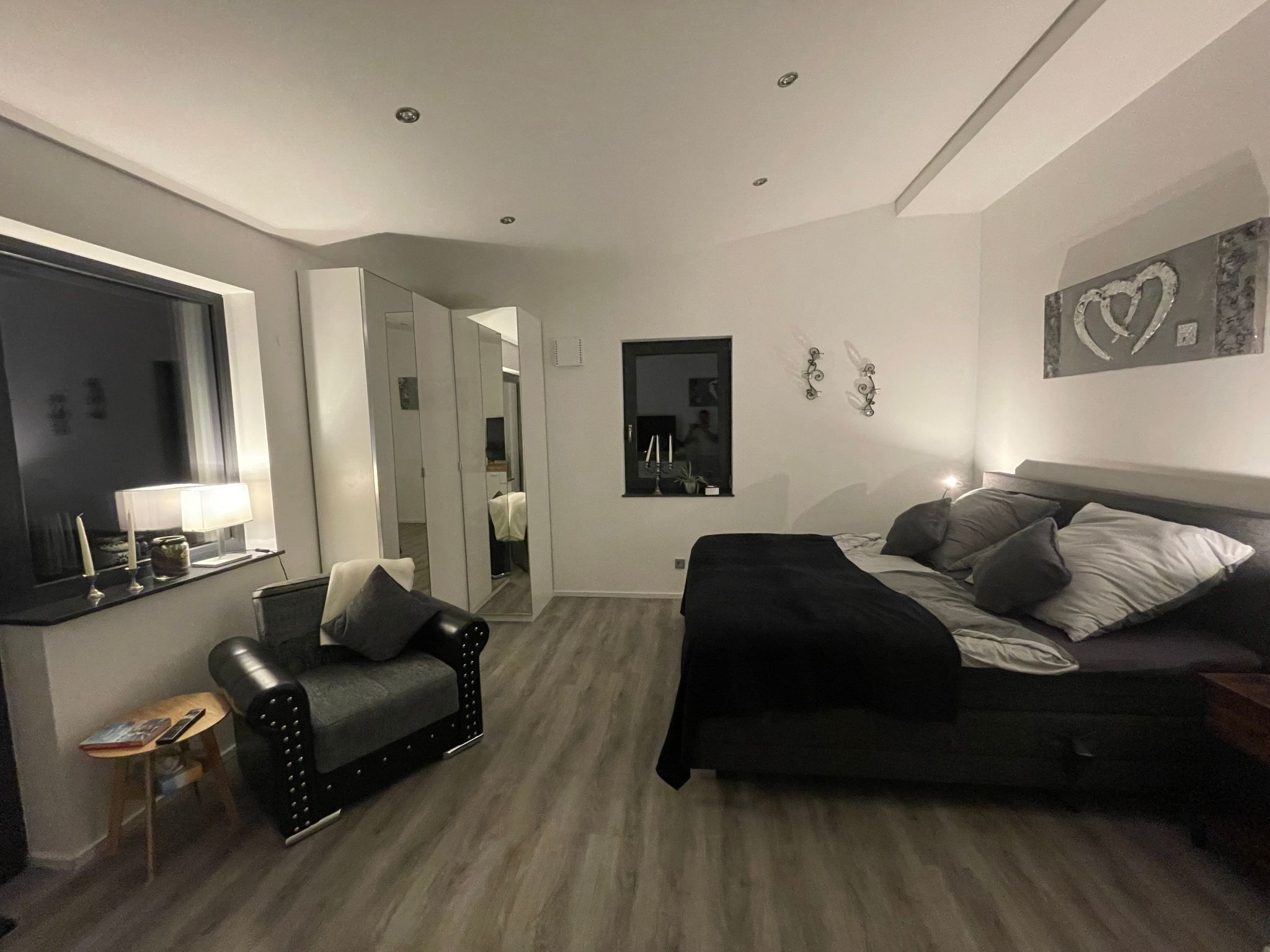 A bedroom with a bed, a chair, a desk, and a mirror.