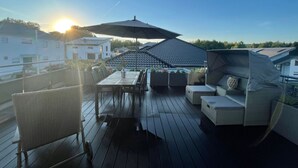 Une terrasse sur le toit, avec une table et des chaises, un grand parasol et une vue sur les bâtiments environnants.