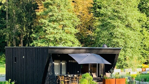Een modern, zwart, gelijkvloers huis met een terras en een zitgedeelte buiten.