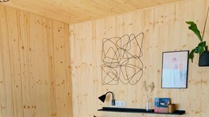 Een kamer met houten lambrisering, een bed, een kunstwerk aan de wand, een plank met decoratieve objecten en een plant.