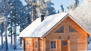 Puinen mökki, jossa on harjakatto, ja sen ympärillä on lumipeitteisiä puita.