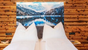 A bed with white bedding and pillows, a painting of a snowy mountain landscape, and a wooden wall with a wooden texture. - Appartement Lee by Interhome (Mauterndorf)