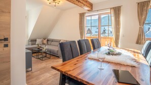 A modern loft bedroom with a sloped ceiling, a dining area with a wooden table, and a sofa. - Appartement Lee by Interhome (Mauterndorf)