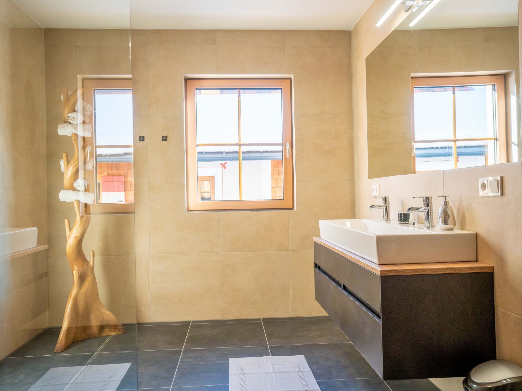 Un baño moderno con un ventanal grande, una escultura de madera, un lavamanos y un inodoro.