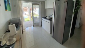Cocina moderna con armarios blancos, refrigerador de acero inoxidable y una puerta corrediza de vidrio que da a un patio.