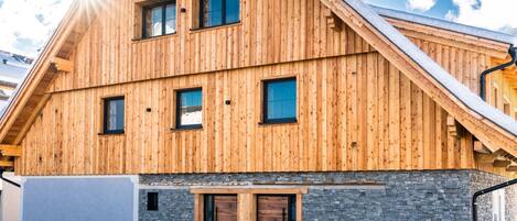 A wooden chalet with a stone foundation, multiple windows, and a sloped roof.