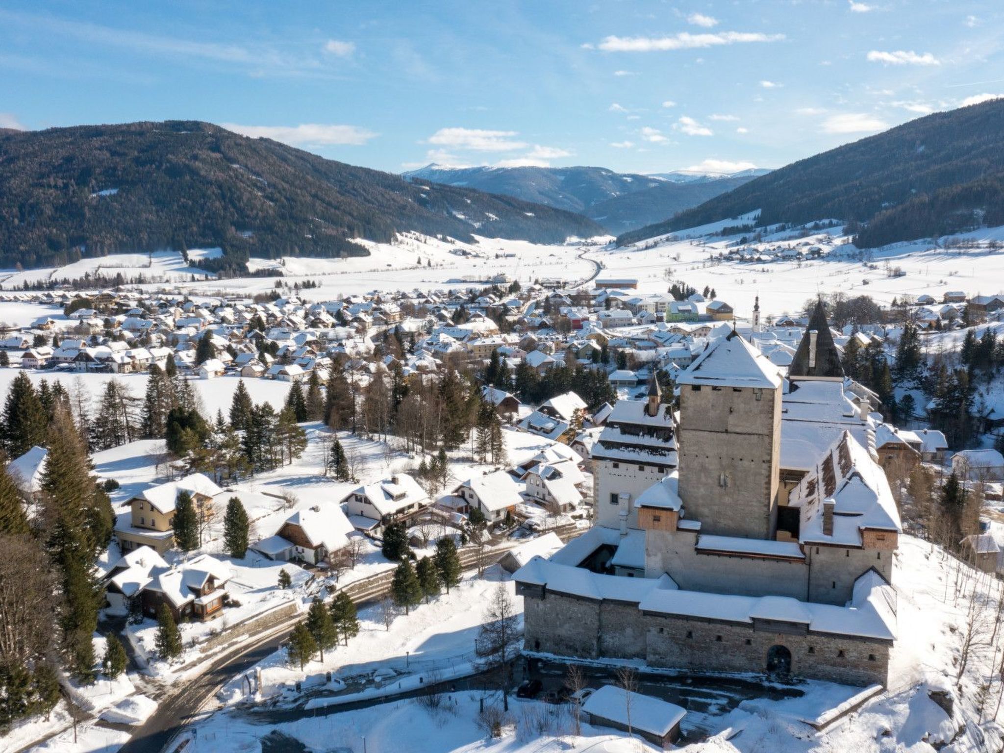 Une ville historique, dominée par un château imposant, entourée de bâtiments enneigés et de montagnes.